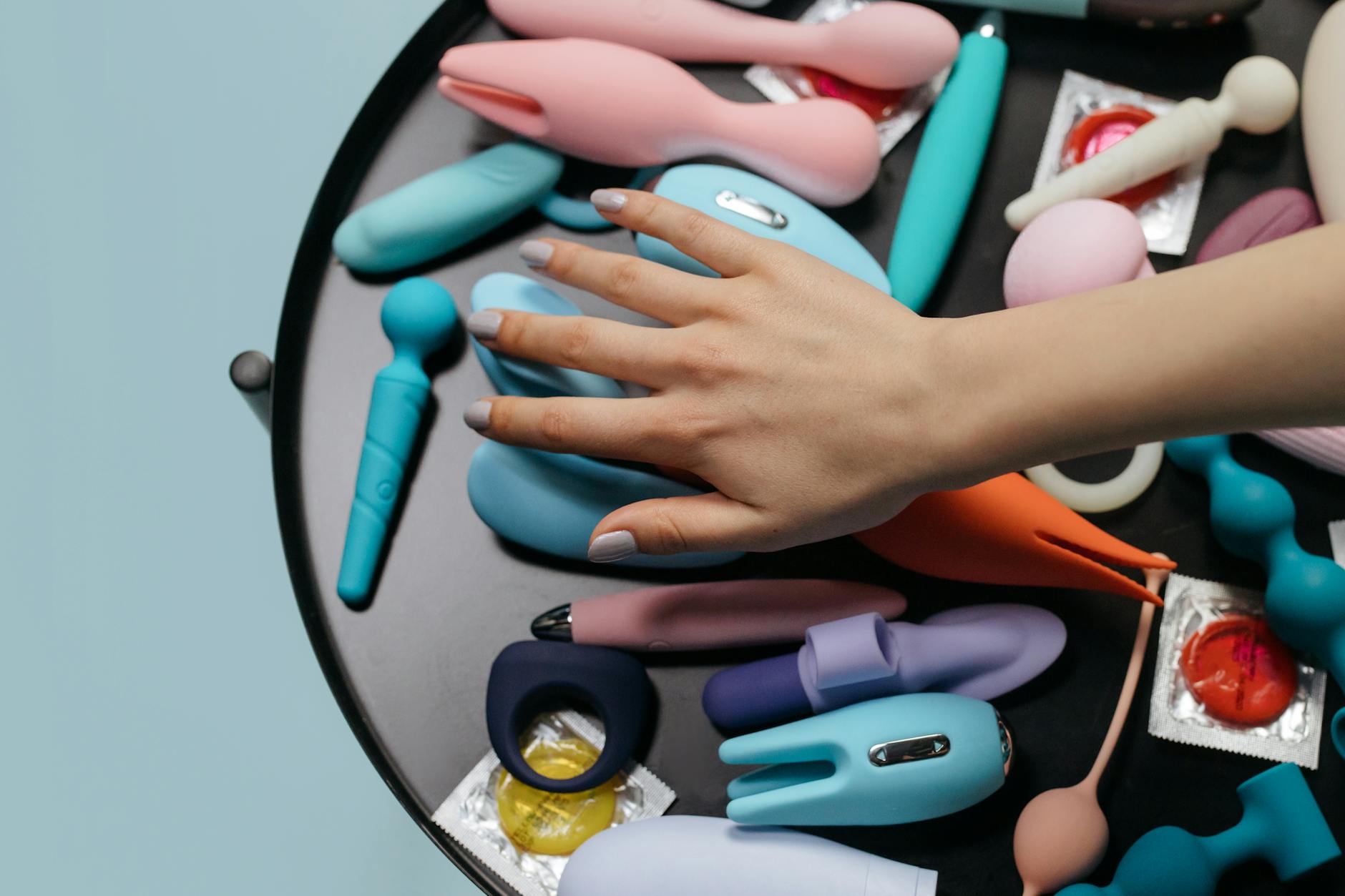 Hand arranging colorful lemon vibrators and adult toys on a neutral surface