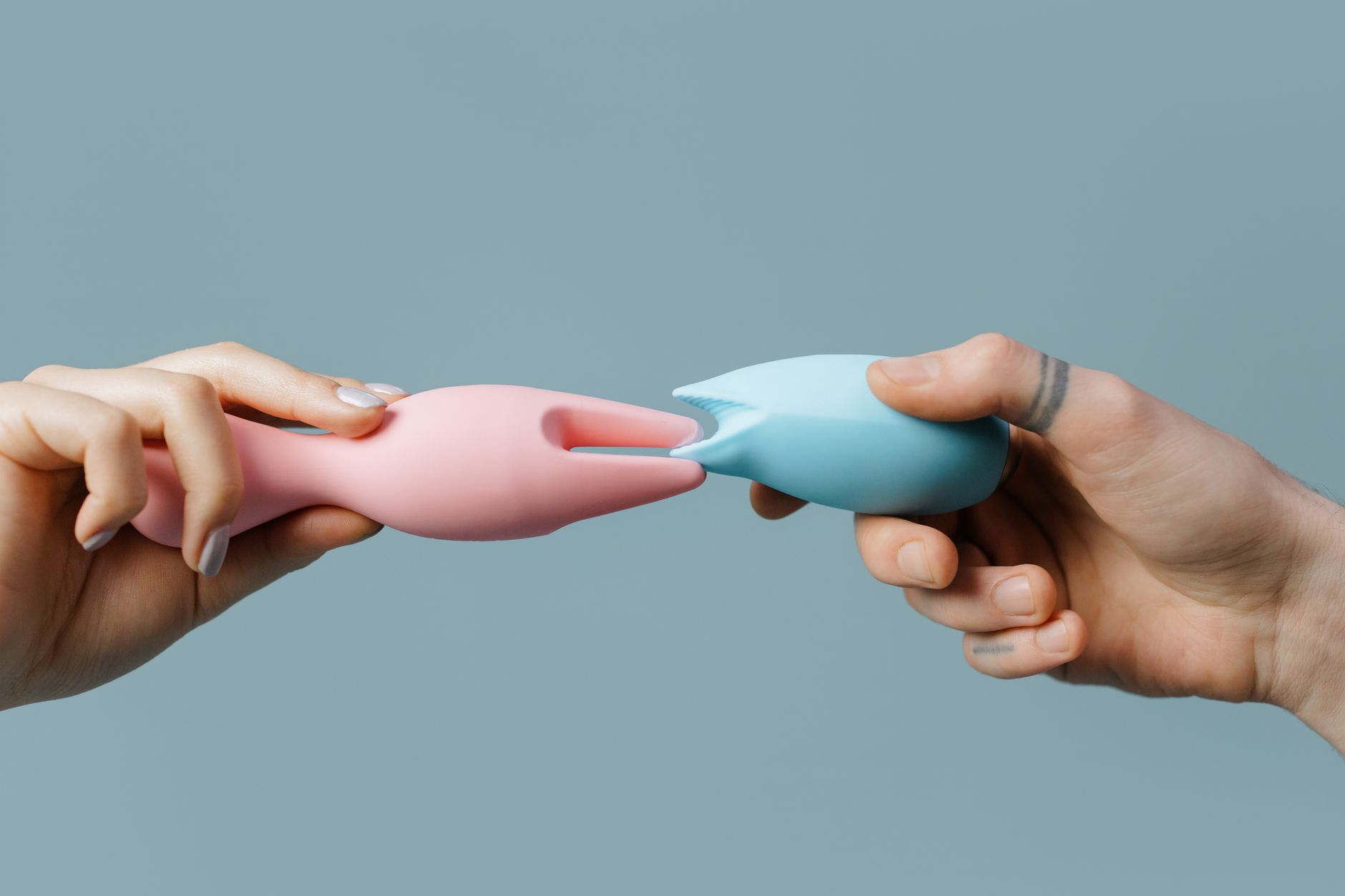 Photo of hands holding colorful vibrators on a pastel background