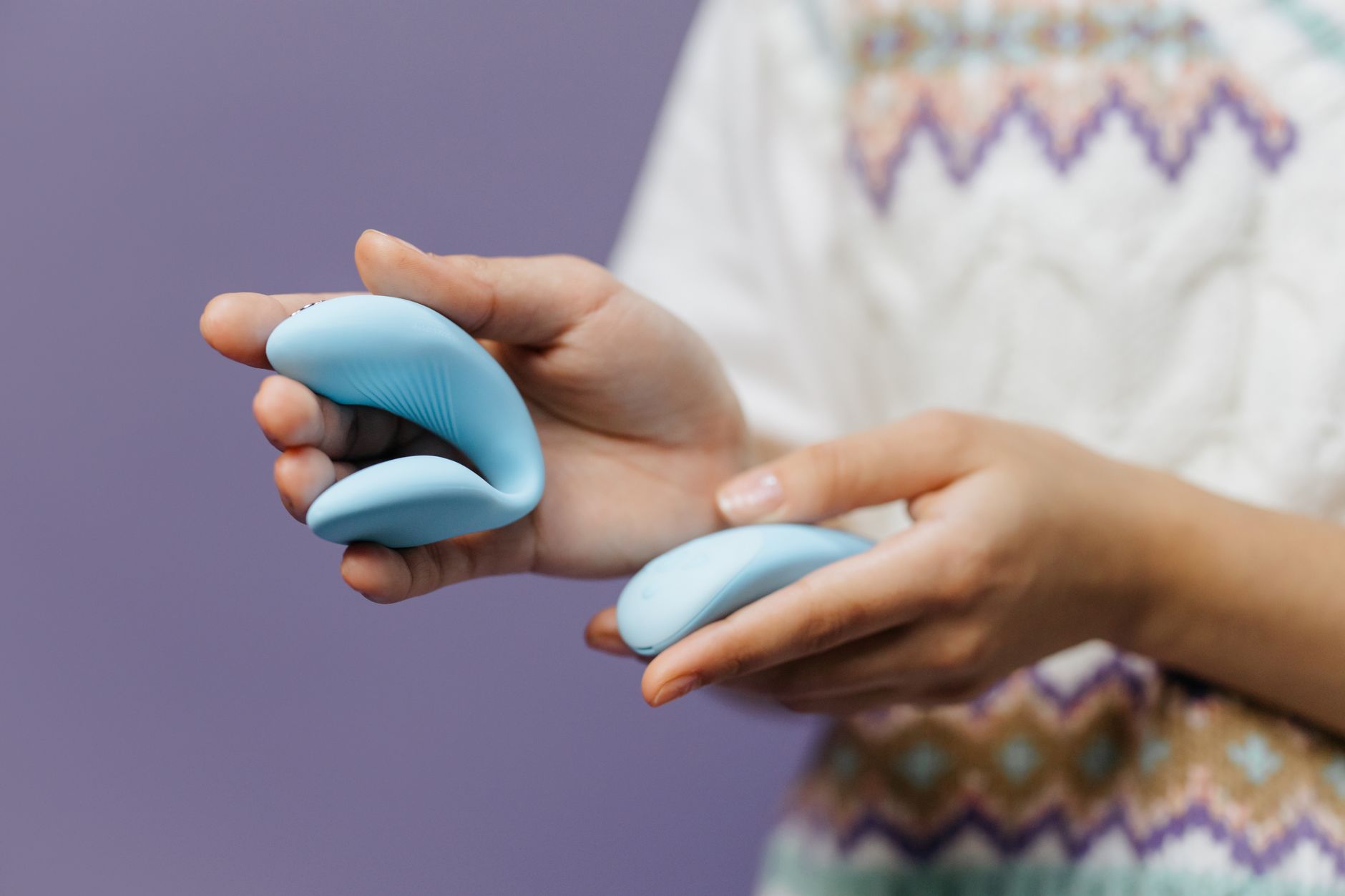 Primo piano delle mani che tengono un elegante vibratore blu su uno sfondo viola.