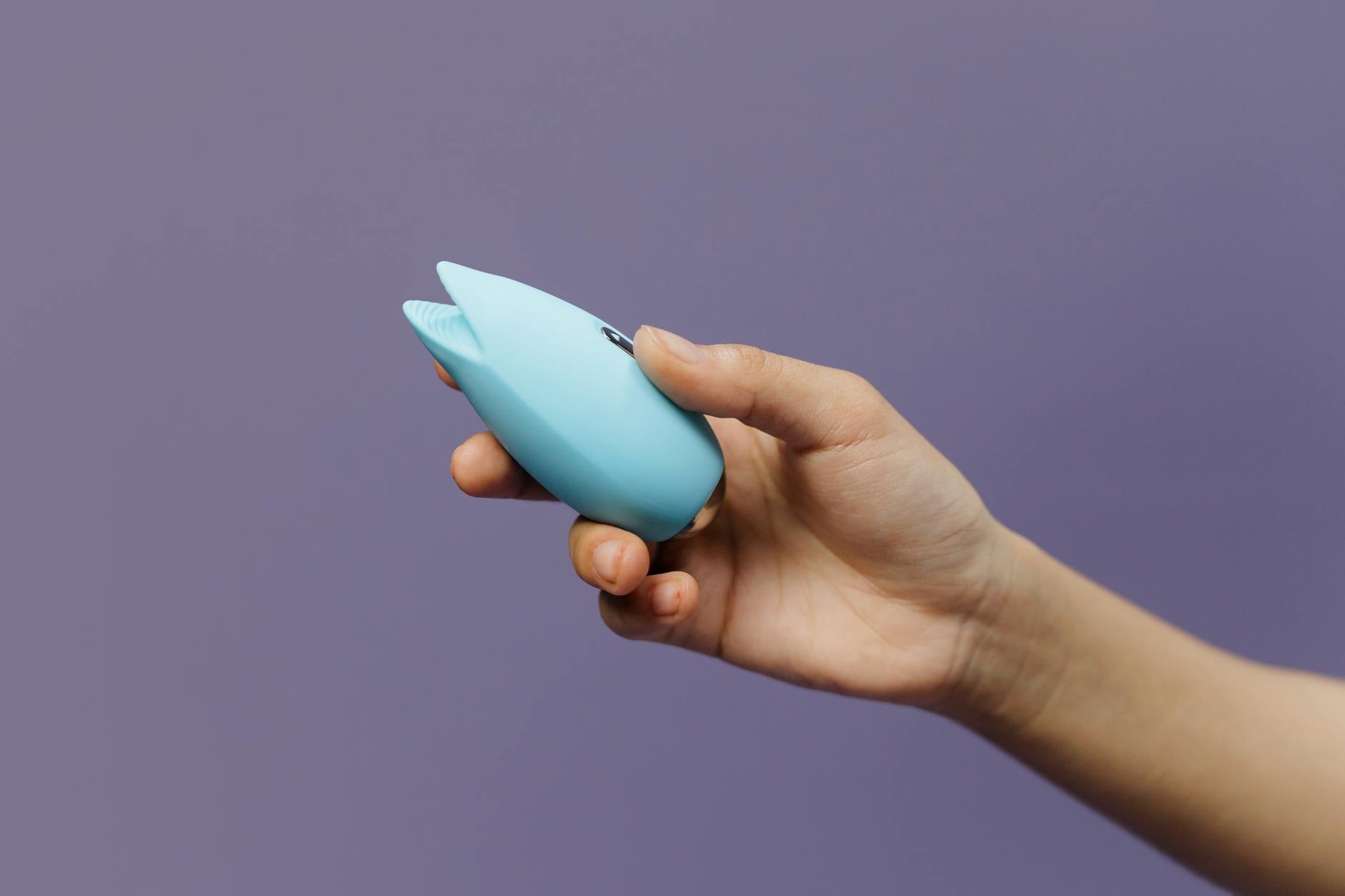 A teal vibrator resting on smooth white silk fabric, suggesting comfort and intimacy