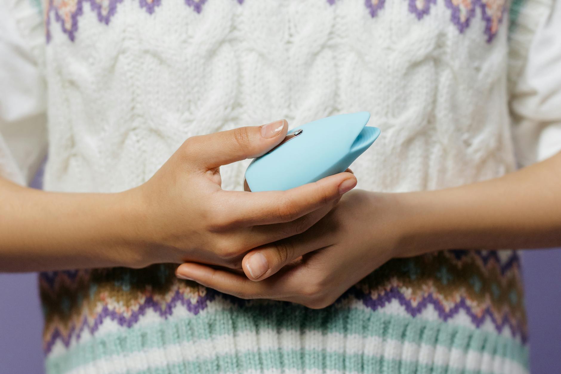 Dettaglio di mani che tengono un vibratore blu contro un maglione di lana