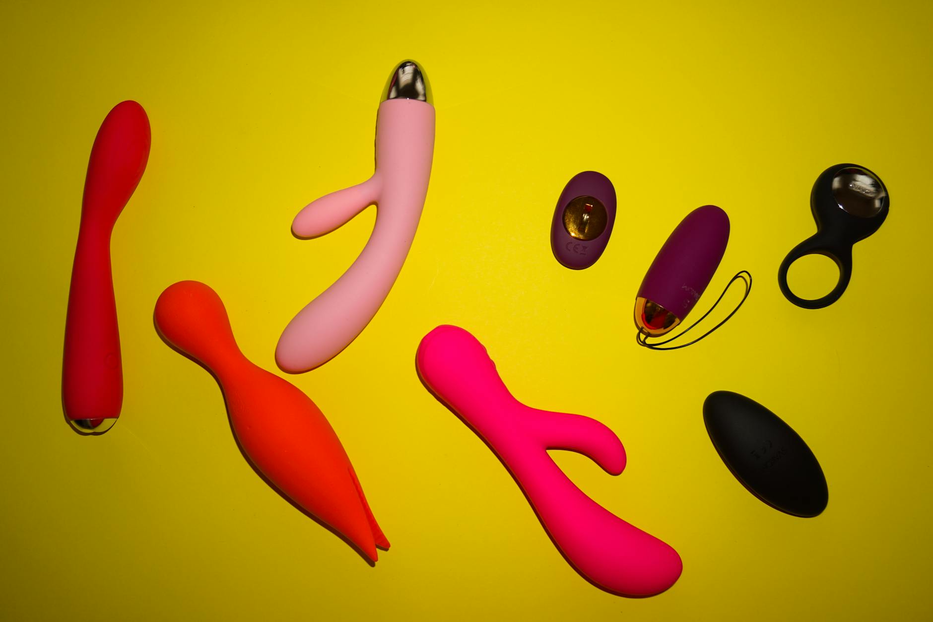Various colorful clitoral vibrators and adult toys arranged on a bright yellow surface