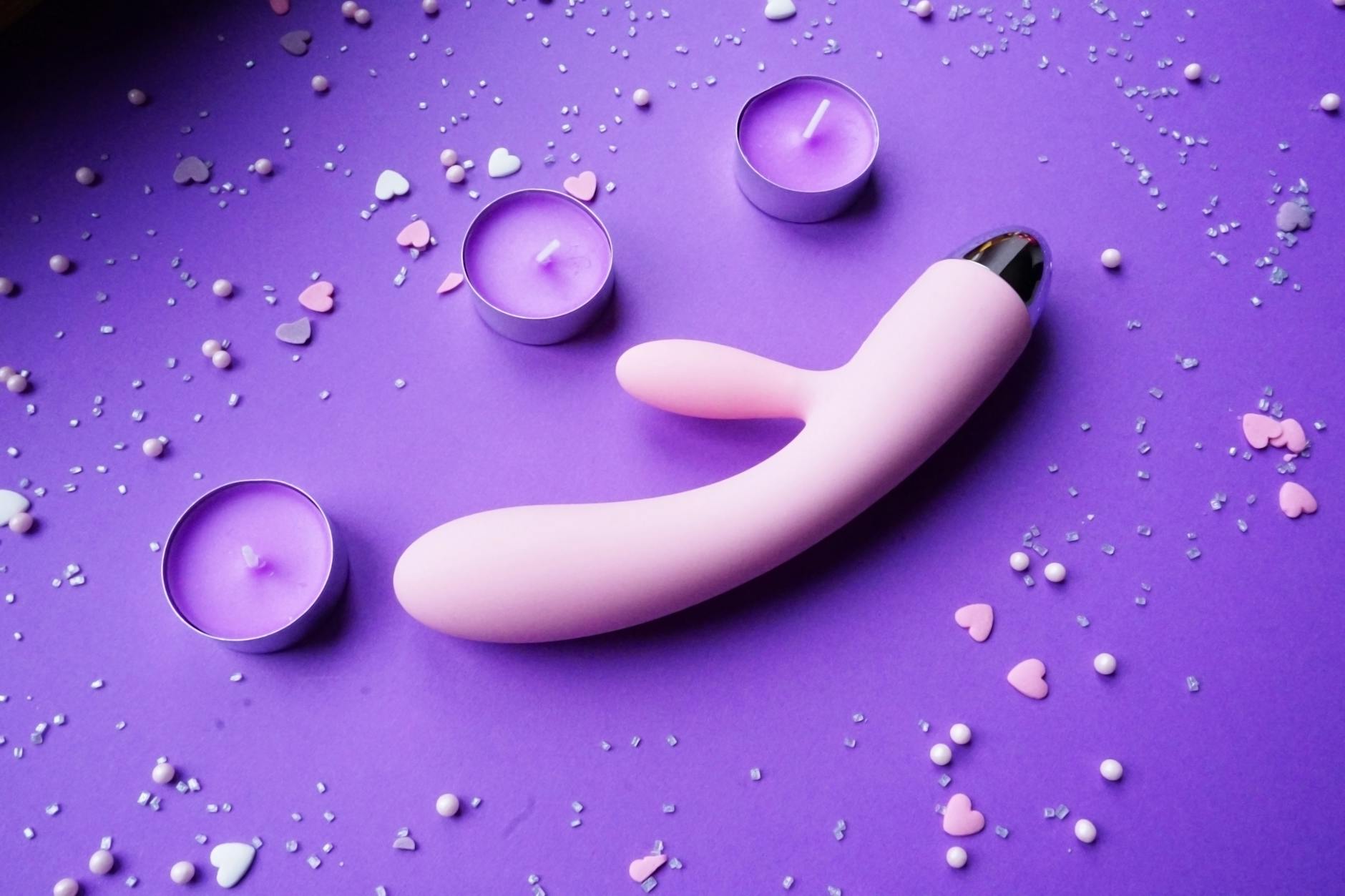 Pink vibrator arranged with flowers and candles on a purple background for intimate connection
