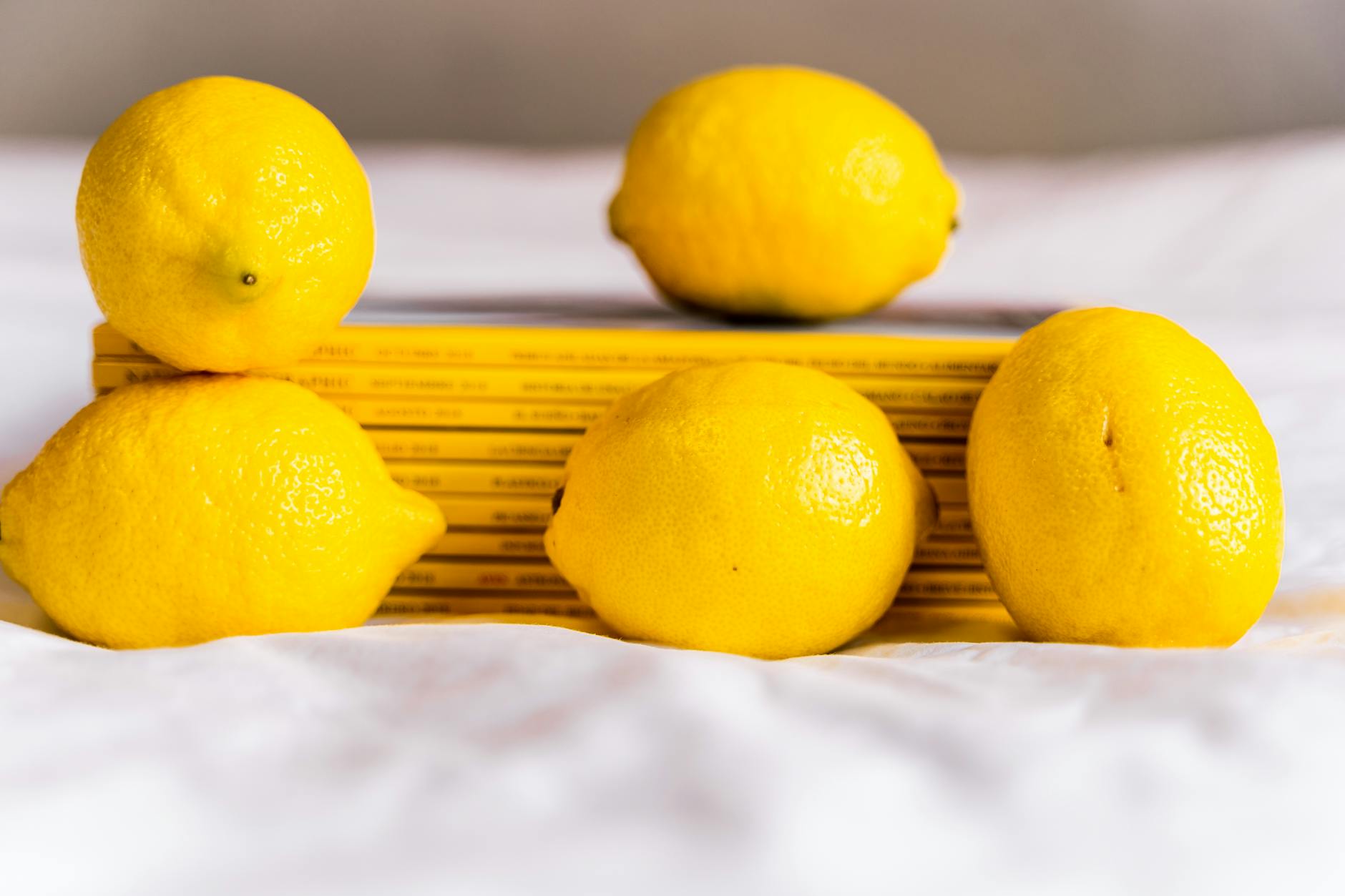 Una composizione con limoni interi freschi e maturi posti insieme a libri impilati su una tovaglia bianca.